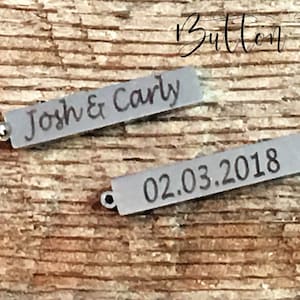 May include: Two silver rectangular tags with engraved text. The first tag reads "Josh & Carly". The second tag reads "02.03.2018".