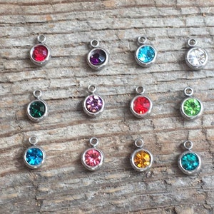 May include: Assortment of 12 small round metal charms with different colored rhinestones. The charms are silver and have a loop at the top for attaching to jewelry or other crafts.