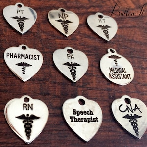 May include: A set of ten silver heart-shaped and round charms with the caduceus symbol and various medical professions engraved on them, including PT, NP, RT, PHARMACIST, PA, MEDICAL ASSISTANT, RN, Speech Therapist, and CNA.