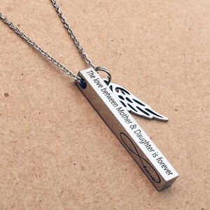 May include: A silver necklace with a bar pendant that reads "The love between Mother & Daughter is forever" and an angel wing charm.