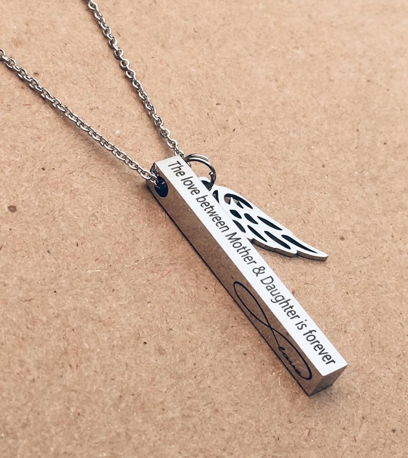 May include: A silver necklace with a bar pendant that reads "The love between Mother & Daughter is forever" and an angel wing charm.