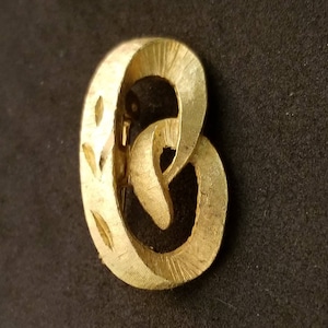 May include: A gold-toned metal brooch in the shape of a stylized letter 'C'. The brooch has a textured surface and a delicate design.