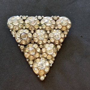 May include: A silver triangle-shaped brooch with a cluster of clear and iridescent rhinestones.