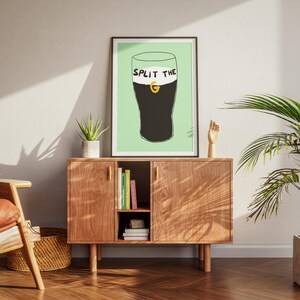May include: A framed print with a green background and a black and white illustration of a glass of Guinness with the text "Split the G" on the glass.