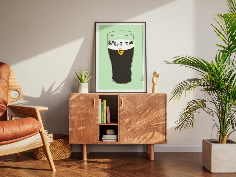 May include: A framed print with a green background and a black and white illustration of a glass of Guinness with the text "Split the G" on the glass.