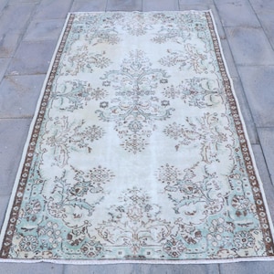 May include: Rectangular vintage rug with a distressed look. The rug features a light blue central field with floral and ornamental patterns in brown and teal. A brown border frames the design.
