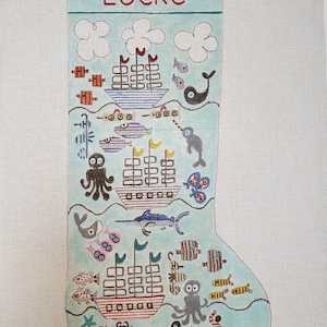 May include: A blue and white stocking with a nautical theme. The stocking features a variety of sea creatures, including fish, an octopus, a narwhal, and a penguin. The stocking is personalized with the name "Locke".