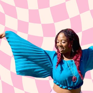 May include: A turquoise blue crop top with pleated, flared sleeves. The top is paired with pink pants. A pendant necklace with a circular pendant hangs around the neck. The background features a pink and white checkered pattern.