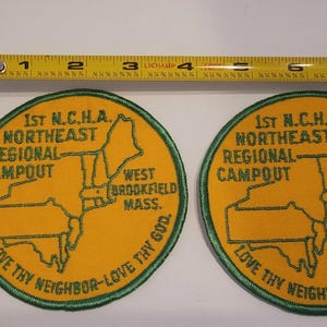 May include: Two round, yellow patches with green embroidered text and a map outline. The text reads "1st N.C.H.A. Northeast Regional Campout, West Brookfield Mass." and "Love Thy Neighbor - Love Thy God."