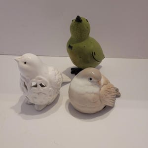 以下が含まれることがあります： セラミック製の鳥の置物3つ。1つは白地にカットアウトのデザイン、1つは薄い茶色でテクスチャ加工が施され、もう1つは緑色のひび割れた釉薬が施されています。