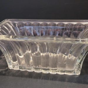 May include: A clear glass rectangular dish with a fluted design. The dish is empty and has a slight curve to the sides.