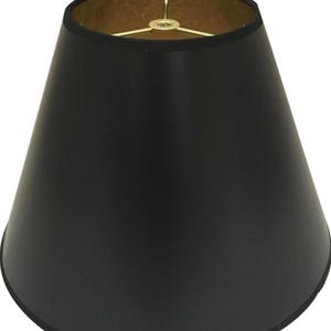 May include: A black lampshade with a conical shape. The lampshade has a smooth, matte finish and a gold-colored interior. The top edge is trimmed with a thin black border. The lampshade is designed to diffuse light.