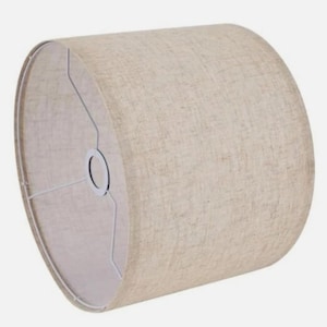 Puede incluir: Pantalla de lámpara cilíndrica con exterior de tela de lino beige. La pantalla tiene una estructura metálica blanca y una abertura circular en la parte inferior. La pantalla está diseñada para difundir la luz.