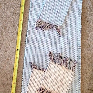 May include: A woven rug and two matching placemats with a fringe trim. The rug is approximately 48 inches long. The rug and placemats have a white and light blue striped pattern.