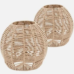 May include: Two woven beige pendant light shades. The shades have a rounded, oval shape and are made of tightly woven natural fibres. The open top and bottom allow for light to shine through. These shades are a decorative element for home lighting.