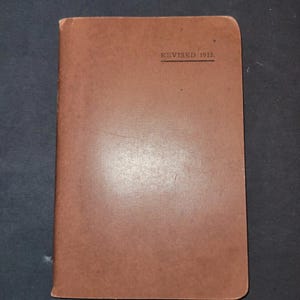May include: A closed, rectangular brown book with rounded corners. The text "REVISED 1913." is printed in black at the top. The cover has a slightly worn appearance.