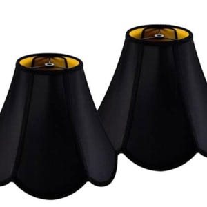 May include: A pair of bell-shaped lamp shades featuring a solid black exterior and a bright yellow interior lining. Each shade has a scalloped bottom edge and a metal spider fitter at the top, designed for standard lamp base attachments.