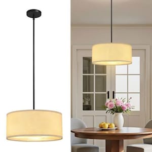 May include: A drum pendant light fitting featuring a cylindrical beige fabric shade suspended by a thin black metal rod. The light emits a warm glow, and the design includes a circular black ceiling canopy at the top of the vertical rod.