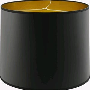 May include: A cylindrical lamp shade featuring a smooth, solid black exterior surface and a metallic gold interior lining. The top opening includes a three-pronged metal spider fitter assembly in a polished gold finish for secure lamp attachment.
