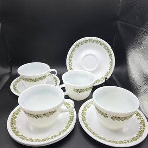 以下が含まれることがあります： 緑色の花柄が施された白いティーカップとソーサーのセット。カップには取っ手があり、ソーサーは丸いです。セットには4つのカップと4つのソーサーが含まれており、お茶やコーヒーを出すのに最適です。