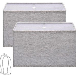 May include: A set of two rectangular lamp shades featuring a textured light grey fabric exterior and a white interior frame. Two metal harps are included, each with a circular base and a vertical wire structure designed for lamp assembly.