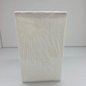 Puede incluir: Un lienzo rectangular blanquecino envuelto en plástico transparente. El lienzo tiene una superficie fina y texturizada. El artículo se presenta sobre un fondo blanco liso.