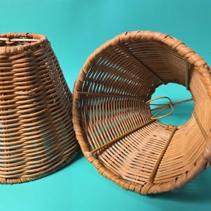 Peut inclure: Deux abat-jours coniques fabriqués en osier tressé brun clair. Chaque abat-jour présente une silhouette effilée avec une ouverture circulaire au sommet et une base plus large. La structure intérieure comprend un cadre en fil métallique.