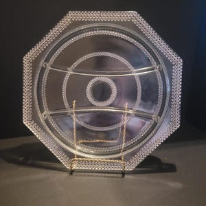 May include: Clear glass serving platter with an octagonal shape and three divided sections. The rim and interior circles are decorated with small, raised dots. The platter is displayed on a gold-colored metal stand, suitable for serving appetizers or snacks.