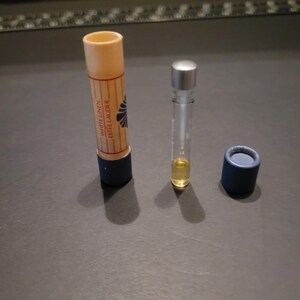 Könnte beinhalten: Ein Parfüm-Proben-Set mit einem kleinen Glasfläschchen mit silbernem Verschluss, einem zylindrischen Behälter mit dem Text "White Linen Estée Lauder" und einer kleinen blauen Kappe. Das Fläschchen enthält eine gelbe Flüssigkeit.