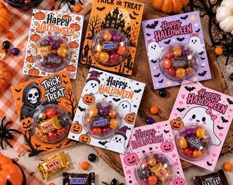 Może przedstawiać: Sześć prostokątnych kart na Halloween z przezroczystymi plastikowymi kopułami zawierającymi różne czekoladki, takie jak Twix, Snickers i M&Ms. Każda karta zawiera świąteczne ilustracje duchów, dyń i nawiedzonych domów z napisami takimi jak Happy Halloween i Trick or Treat.