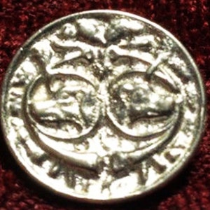 May include: Silver coin with a design of two intertwined animals with their heads facing each other. The coin has a raised rim and a smooth surface.