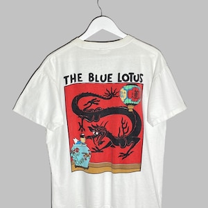 May include: White t-shirt featuring a graphic from "The Blue Lotus." The design includes a black dragon, a colorful lantern, and a decorative vase on a red background. The text "THE BLUE LOTUS" is printed above the graphic.