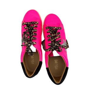 May include: A pair of pink sneakers with black trim and leopard print laces. The sneakers have a silver star on the side.