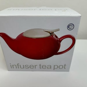 May include: A red ceramic infuser tea pot with a silver lid and a gold handle. The tea pot is on a white box with the text "infuser tea pot" printed on it.