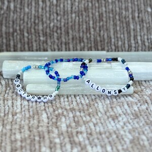 May include: Three beaded bracelets with the words "DOCTOR WHO" and "ALLONS-Y" spelled out in black letters on white beads.
