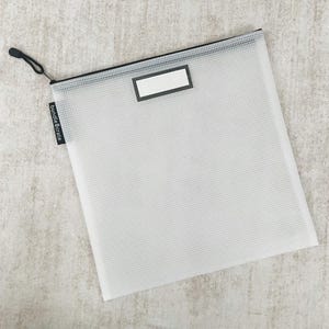 May include: A clear, square, zippered document pouch with a grid pattern. The pouch has a black zipper, a black pull cord, and a small black tag that reads "bundlecrate." A white rectangle is on the front of the pouch.