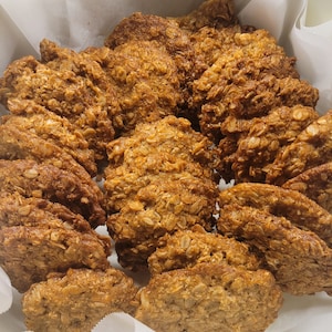 May include: A basket of golden-brown oatmeal biscuits. The biscuits are round and have a textured surface, with visible oats and a slightly crispy appearance. They are arranged on white parchment paper.