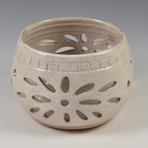 May include: A white ceramic bowl with a decorative cut-out design. The bowl has a speckled glaze and a raised rim.