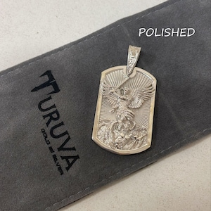 May include: A silver pendant featuring a detailed depiction of an angel with wings spread, holding a sword, and standing over a dragon. The pendant is in the shape of a dog tag and has the word "POLISHED" printed on the background.