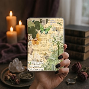 May include: A rectangular phone case featuring a collage of vintage-style botanical illustrations, including a green butterfly, white flowers, and a small ghost. The background has aged paper text and the phrase, You are my sun, my moon, and all of my stars.