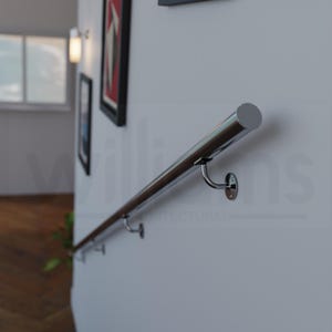 May include: A polished chrome handrail mounted on a white wall. The handrail is cylindrical and supported by curved brackets. The image also shows framed artwork and the text "Williams Architectural".
