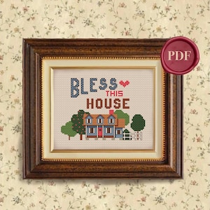 May include: Framed cross-stitch artwork with the words "BLESS THIS HOUSE" above a stitched image of a house, trees, and a white picket fence. The text and house are in shades of blue, red, green, and brown. The frame is a dark wood color.