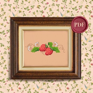May include: A cross-stitch pattern featuring a red strawberry with green leaves and white flowers. The pattern is framed in a brown wooden frame with a cream-coloured mat. The image includes the word "PDF" in a red wax seal.