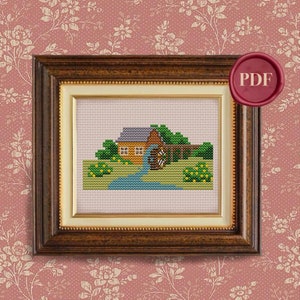 May include: A cross-stitch pattern of a small brown house with a green roof and a water wheel. The house is surrounded by green trees and bushes. The pattern is framed in a brown wooden frame.