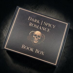 May include: A rectangular black cardboard box featuring gold-colored text that reads DARK | SPICY ROMANCE BOOK BOX. The center of the lid displays a graphic illustration of a human skull with a red rose in its teeth, framed by a thorny heart shape.