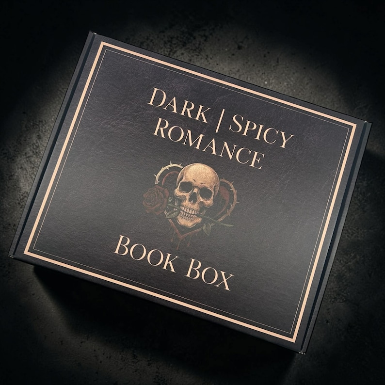 May include: A rectangular black cardboard box featuring gold-colored text that reads DARK | SPICY ROMANCE BOOK BOX. The center of the lid displays a graphic illustration of a human skull with a red rose in its teeth, framed by a thorny heart shape.