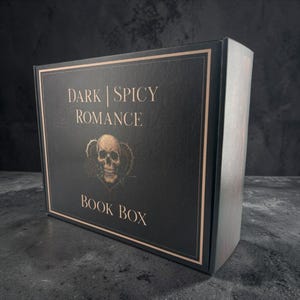 May include: A rectangular black cardboard box with copper-colored text and a border. The front features the text "DARK | SPICY ROMANCE" above a graphic of a human skull with a rose in its mouth, centered over a heart, with "BOOK BOX" below.
