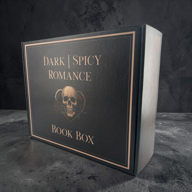 May include: A rectangular black cardboard box with copper-colored text and a border. The front features the text "DARK | SPICY ROMANCE" above a graphic of a human skull with a rose in its mouth, centered over a heart, with "BOOK BOX" below.