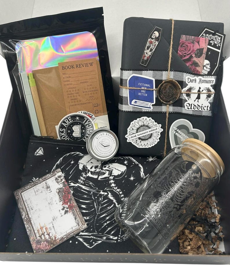 May include: A gift box containing a book wrapped in black paper with stickers and a wax seal, a glass tumbler with a bamboo lid, a black zippered pouch with a skeleton print, a book review notebook, a small metal tin, and a holographic pouch.