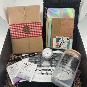 May include: A gift box filled with book-themed items. Includes a wrapped book with a red and white checkered ribbon, a pen, tea bags, a candle, a glass jar, and a tote bag with the text "My weekend is all booked."